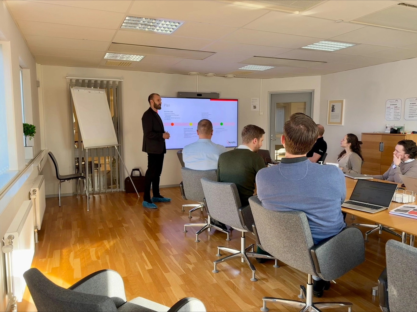 Man presents a 'Plan' on screen to people at a meeting table.