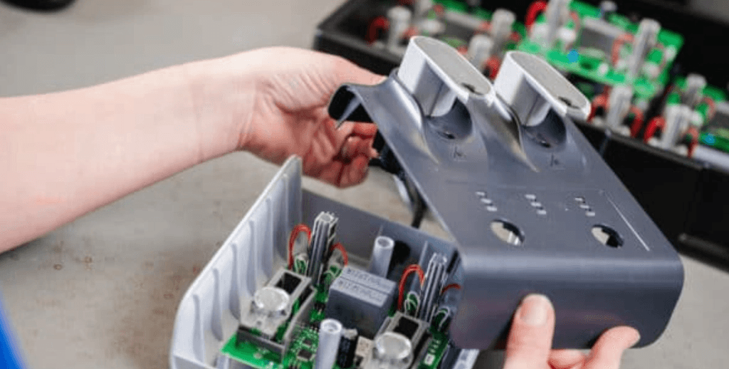 Hands assemble an electronic device, placing a gray cover with openings onto visible green circuit boards and components.