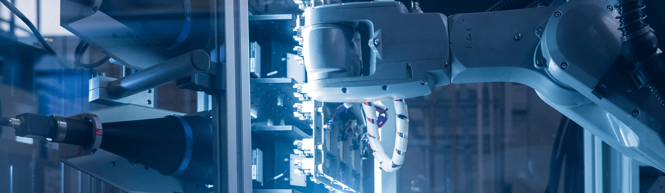 Automated robotic arms working in a brightly lit, blue-hued factory setting.