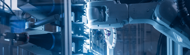 Automated robotic arms working in a brightly lit, blue-hued factory setting.
