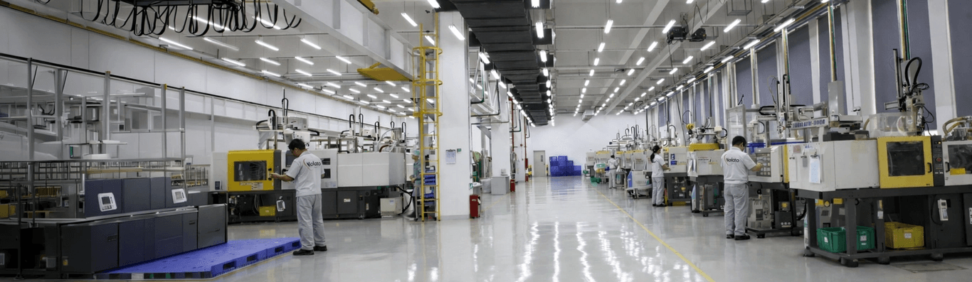 Bright, clean factory with rows of plastic injection molding machines. Workers in uniform operate the equipment.