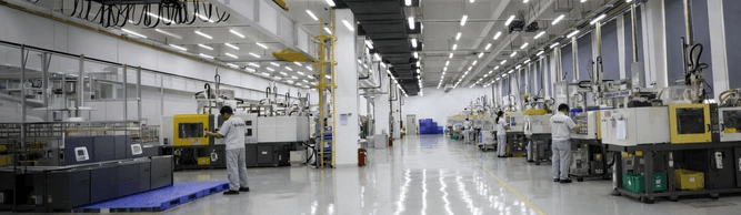 Bright, clean factory with rows of plastic injection molding machines. Workers in uniform operate the equipment.