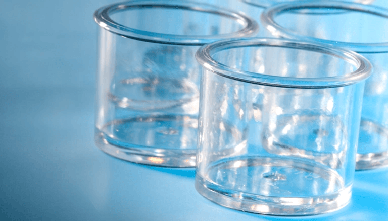 Several clear, empty glass cylindrical containers with thick bottoms and flared rims, on a blue surface.