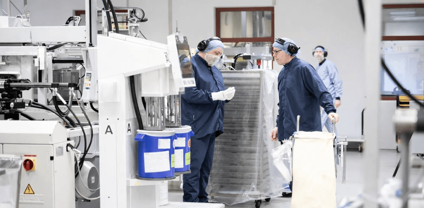 Two operators work at a machine in a cleanroom environment.