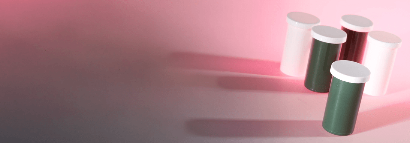 Five cylindrical containers with white lids: two green, two white, and one dark red, on a pink and grey background.