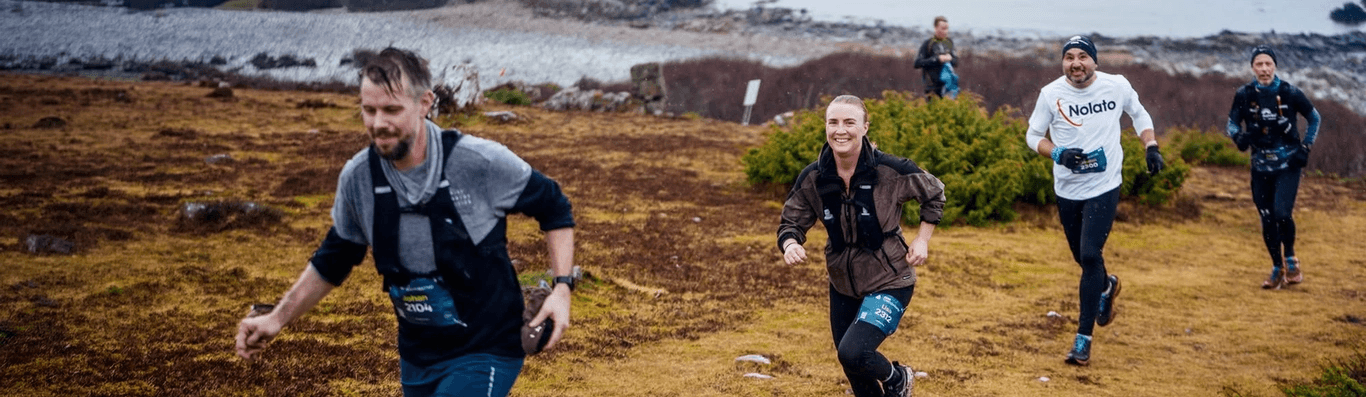 Five trail runners on a rugged, brown landscape beside a lake under a grey, cloudy sky.
